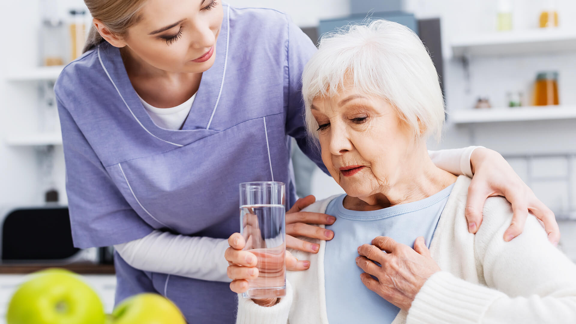 Pflegekraft von Seniorenbetreuung Ziegler reicht einer Seniorin ein Glas Wasser